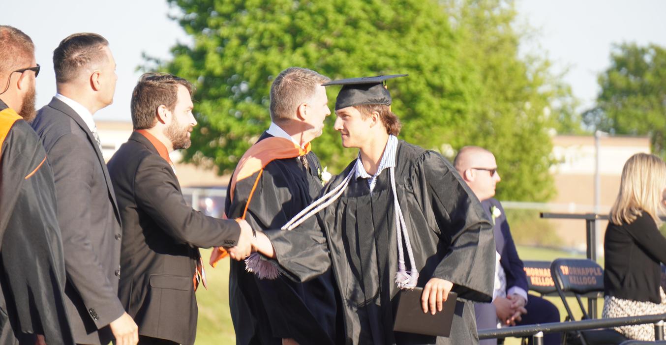 Graduation ceremony with a student receiving a diploma and shaking hands.
