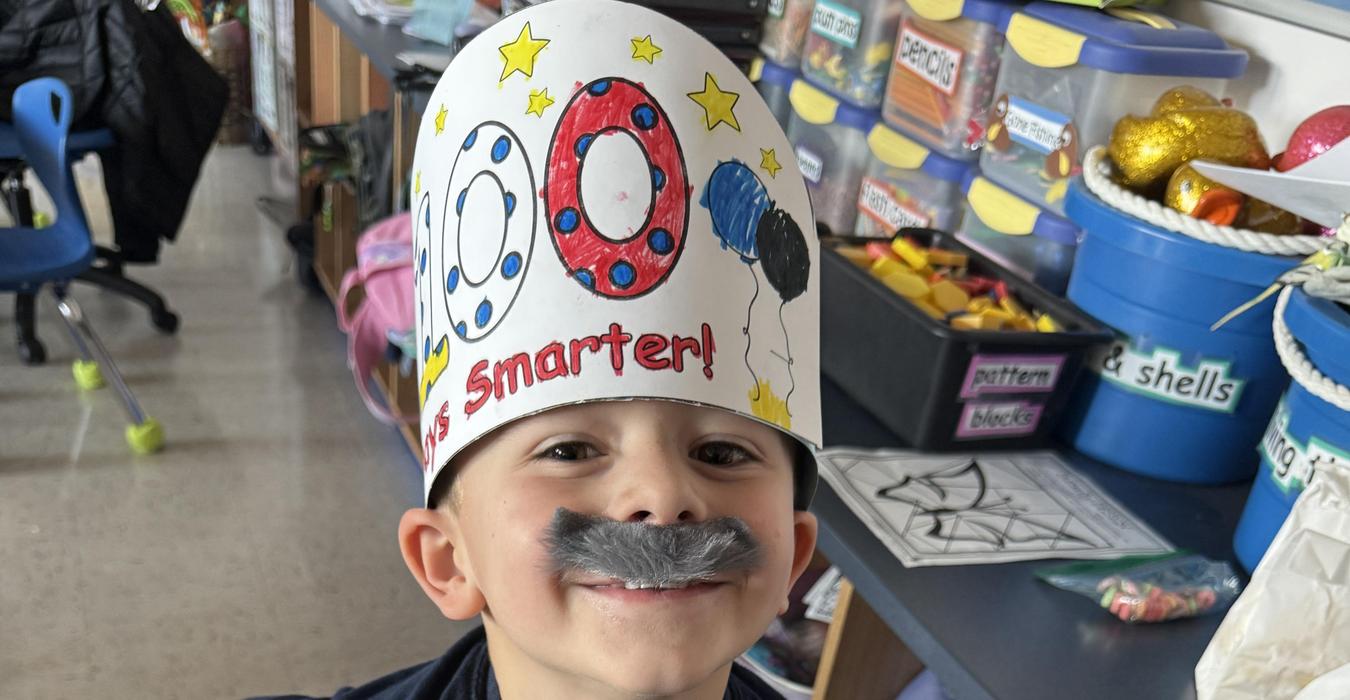 A child with a fake mustache smiling while holding a toy gun.