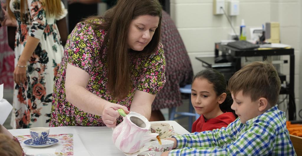 A teacher pours tea into a student's cup.