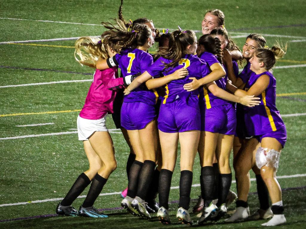 The High School Girls Varsity soccer team hugging in a huddle and celebrating on the field after a win.