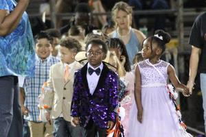 Children in formal wear participate in an event parade.