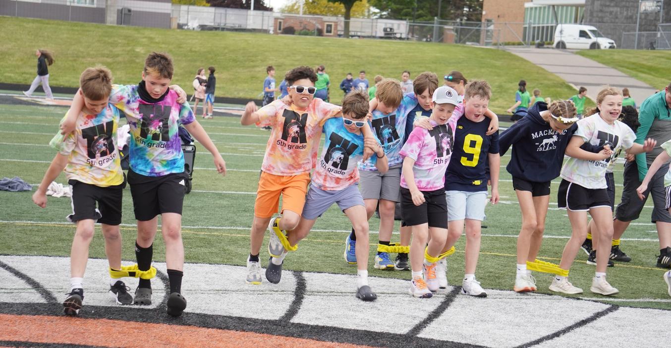 Children in colorful T-shirts participating in a three-legged race on a sports field.