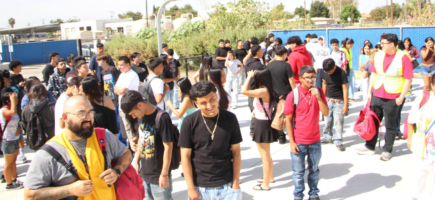 A large group of people gathering outdoors near a basketball hoop.