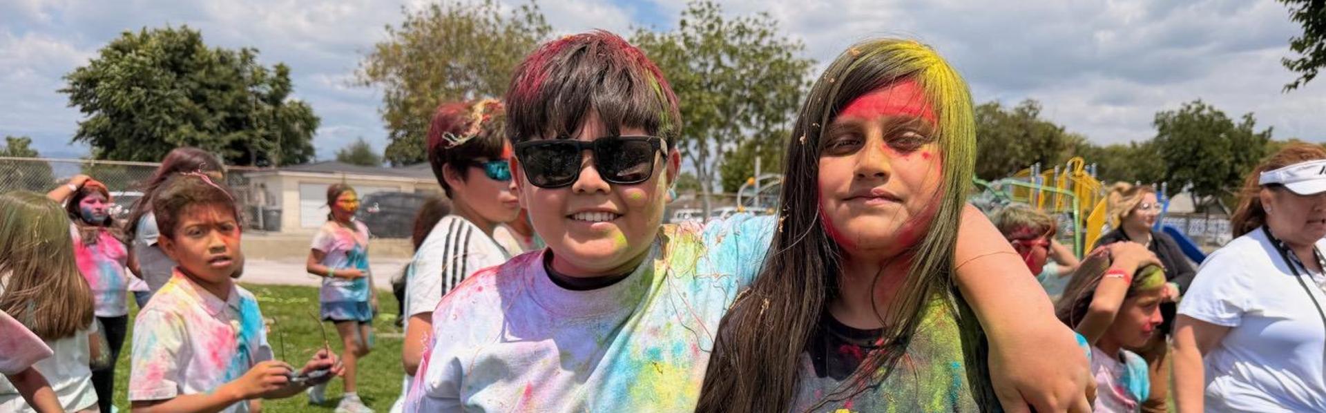 Two smiling children with colorful faces and shirts at a fun outdoor event.