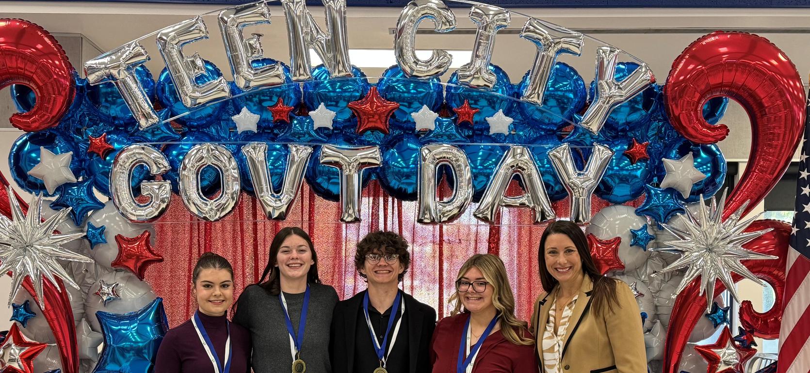 Group of five students at an event, smiling in front of a festive backdrop with stars and balloons.