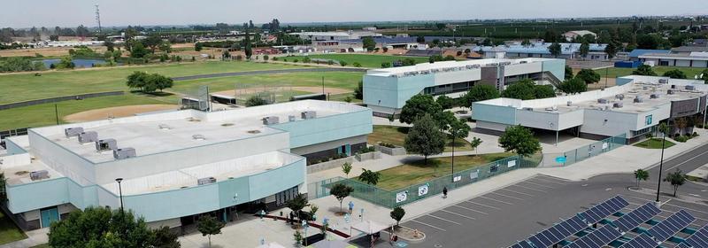 Aerial view of Harmony Magnet Academy's modern campus buildings, open fields, and solar panel-covered parking lot in Strathmore, California.