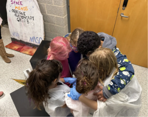A team of elementary students in a huddle in a hallway at the Odyssey of the Mind competition.
