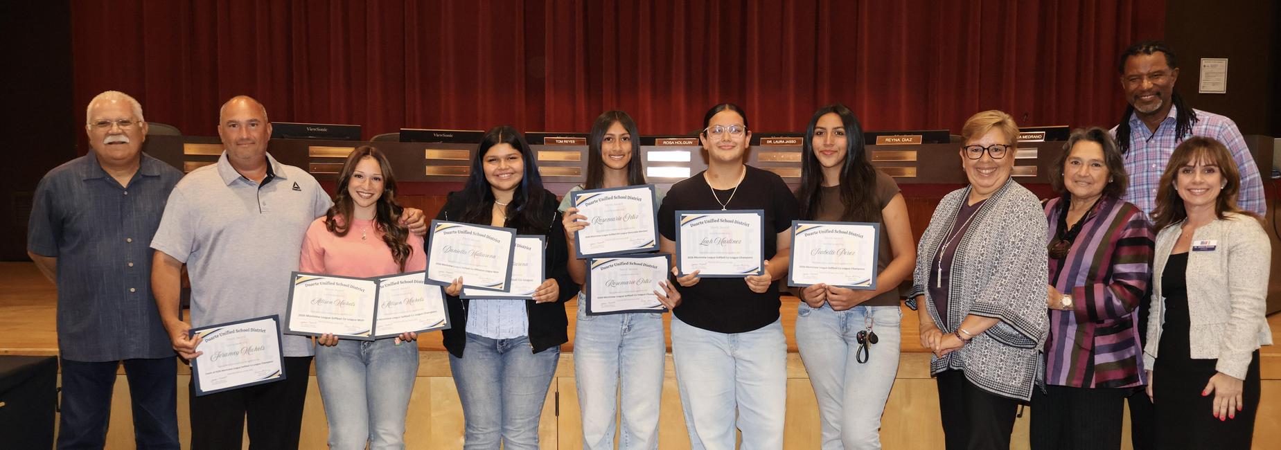 Group of people holding achievement certificates on a stage.
