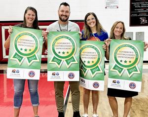 Four principals stand with banners indicating they earned CDE awards.