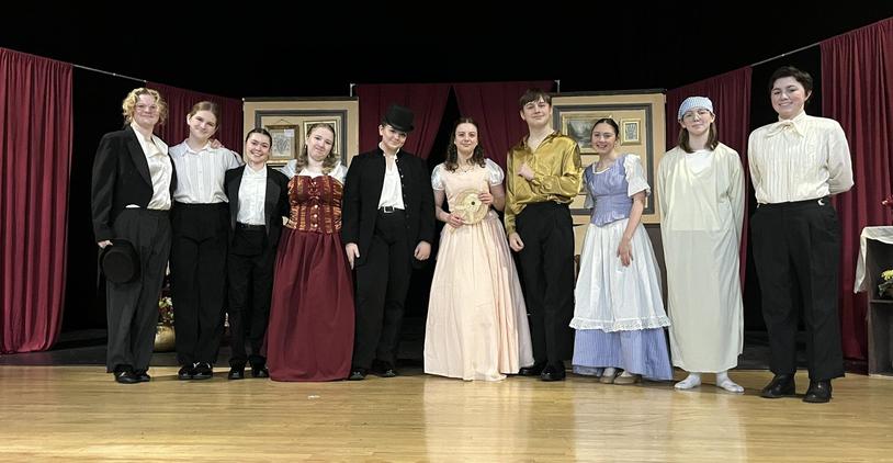 A theatrical performance cast in historical costumes on a stage with red curtains.