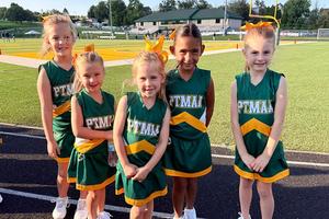 Five young girls dressed in cheer uniforms stand on a football field