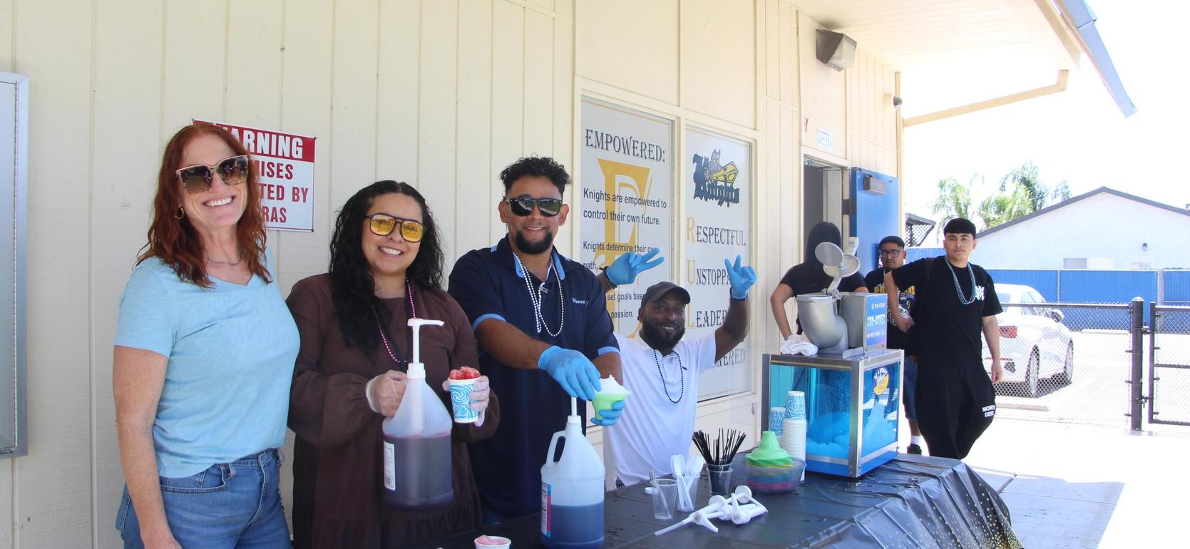 Group of people at a stand serving colorful icy treats.