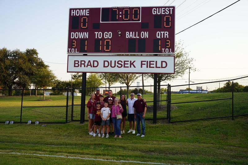 Brad Dusek's family poses under the scoreboard bearing his name