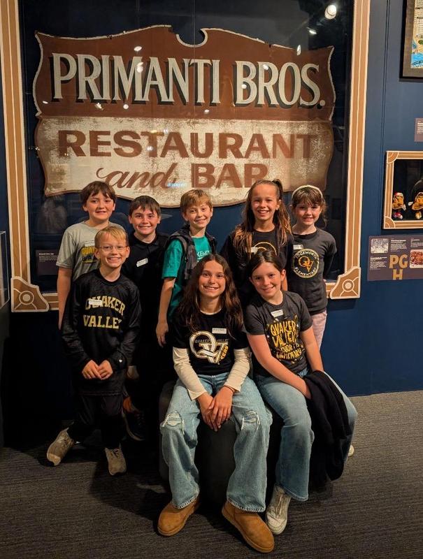 Image depicts a team of Quaker Valley students posing in front of a Primanti Bros. sign at the Heinz History Center.
