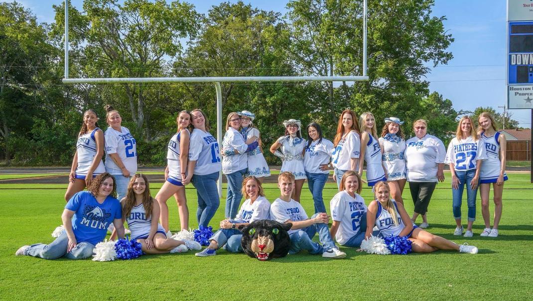 Group of cheerleaders and drill team members posing on a football field.
