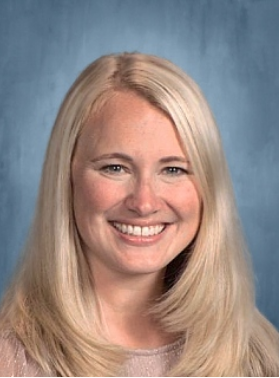 Headshot of a smiling woman with shoulder-length blonde hair, wearing a sparkly top against a textured blue background.