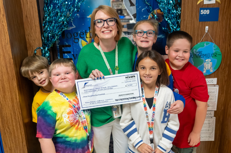 Gifted & Talented Teacher surrounded by students and holding a teacher grant.