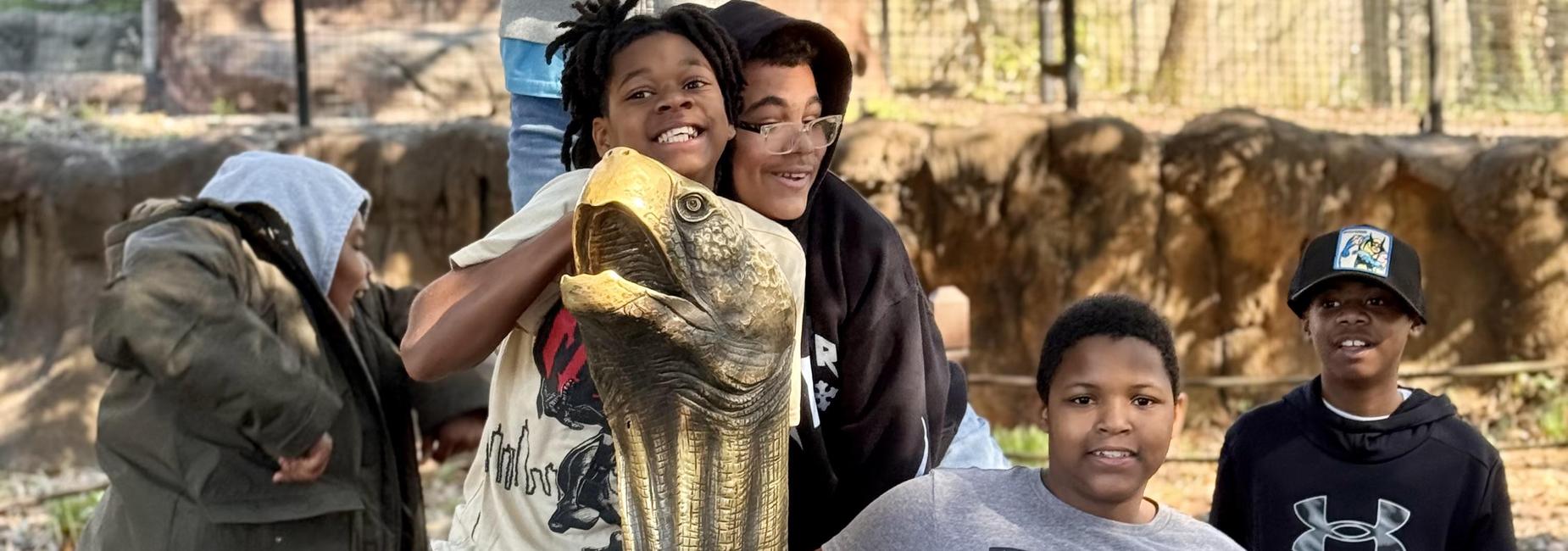 Four children posing happily with a large fish statue in a zoo setting.