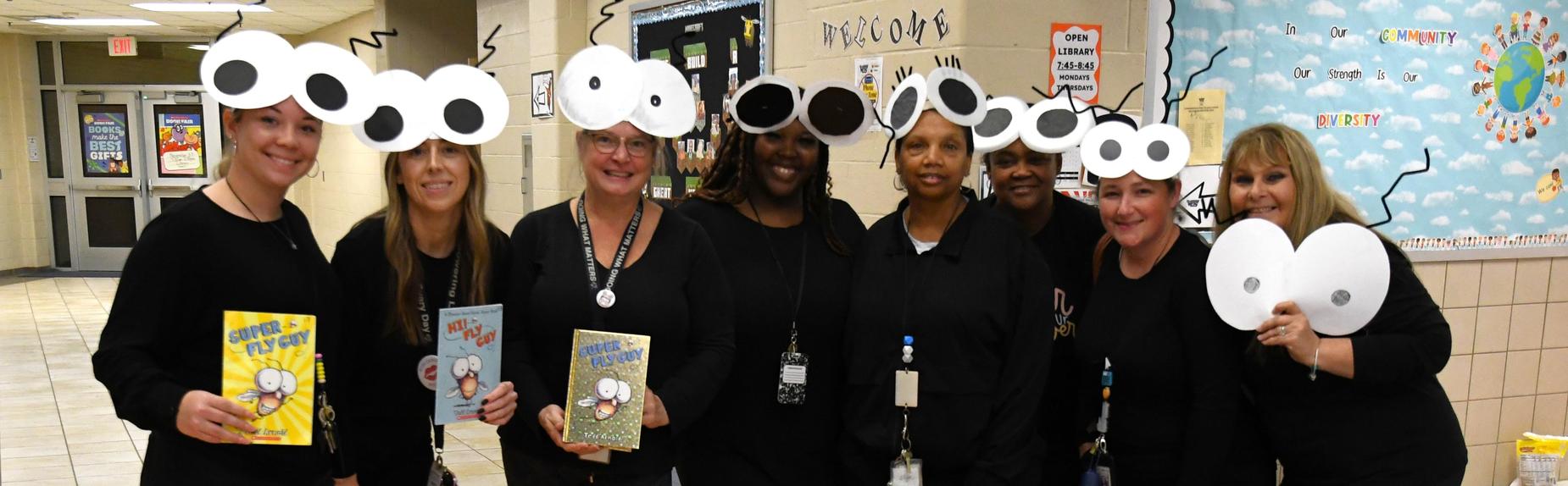 A group of smiling women wearing black shirts with cartoonish eyes drawn on their heads.