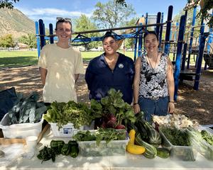 a man and two women stand in front of a table fllled with fresh produce