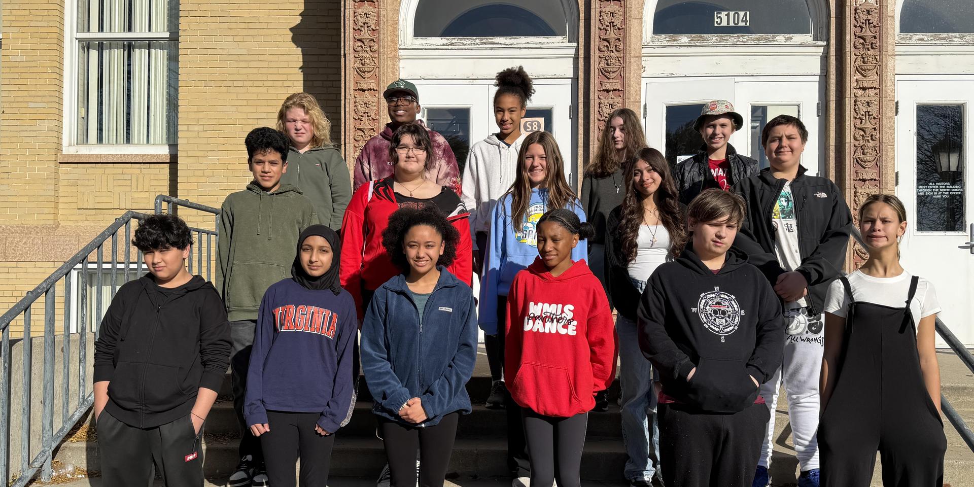 A diverse group of 16 people standing on steps in front of a building.