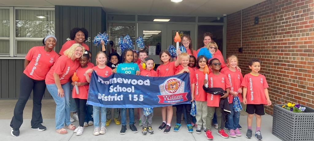group of students and adults pose with Willow School banner