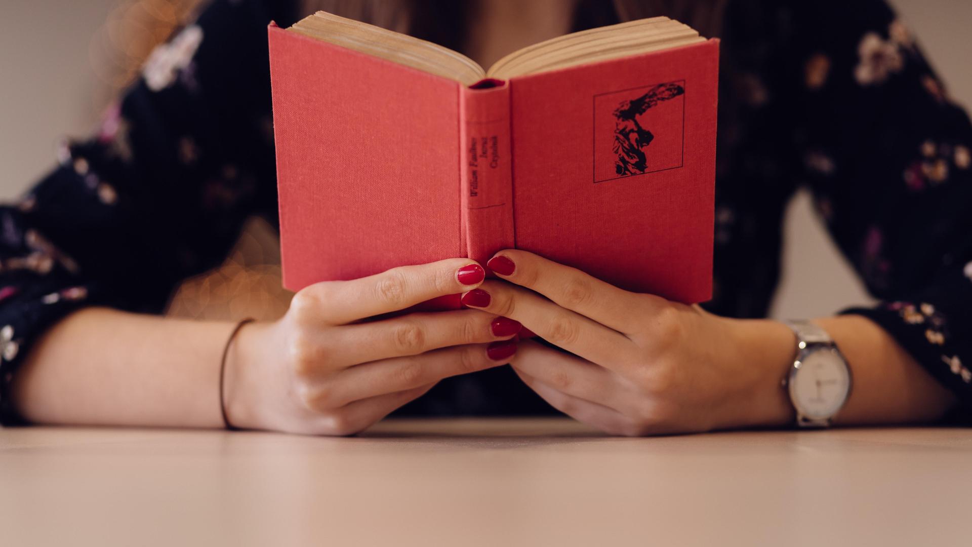 A person holding a red book with a floral background.