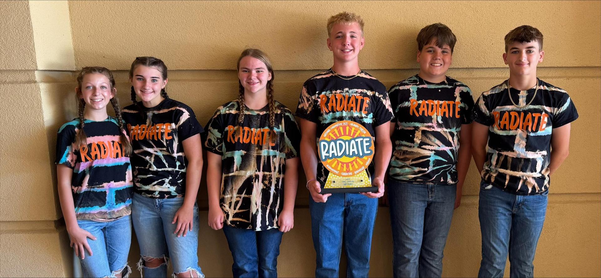 Six students in front of a wall holding a Radiate trophy. 