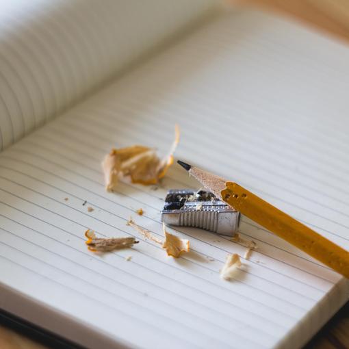 A sharpened pencil and sharpener on an open notebook with shavings.