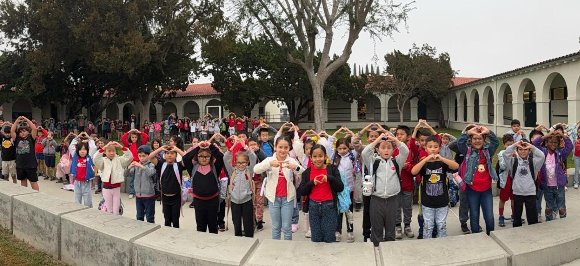 A crowd of students lined up outdoors making hand gestures.