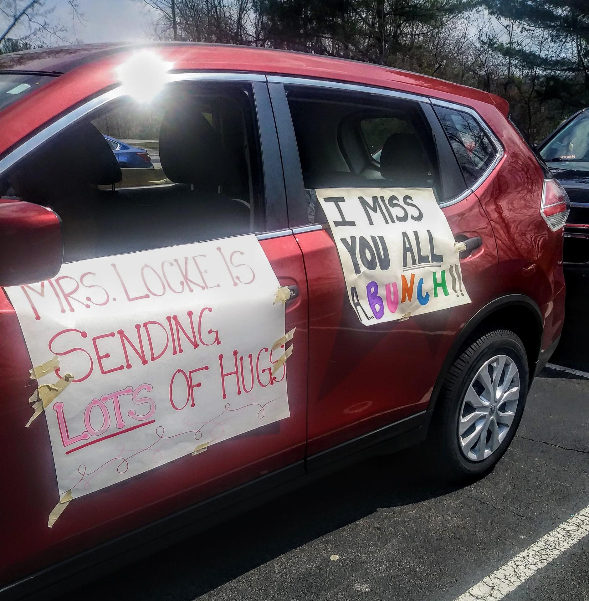 Car with posters saying "Mrs. Locke is sending lots of hugs" and "I miss you all a bunch"