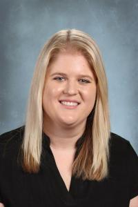 Smiling woman with blonde hair and black blouse, set against a blue background.