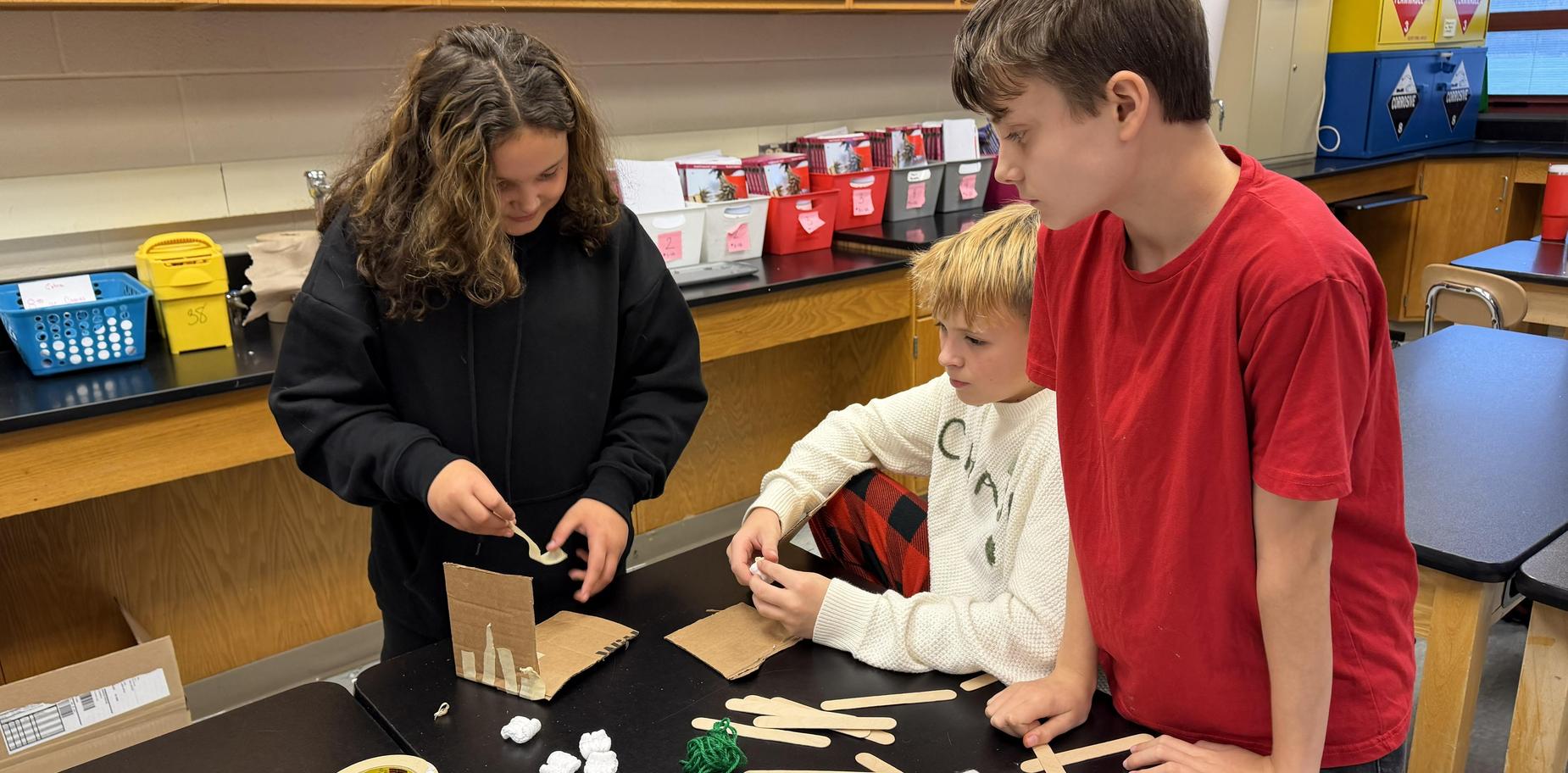 Three students assembling a craft project together at a classroom table.