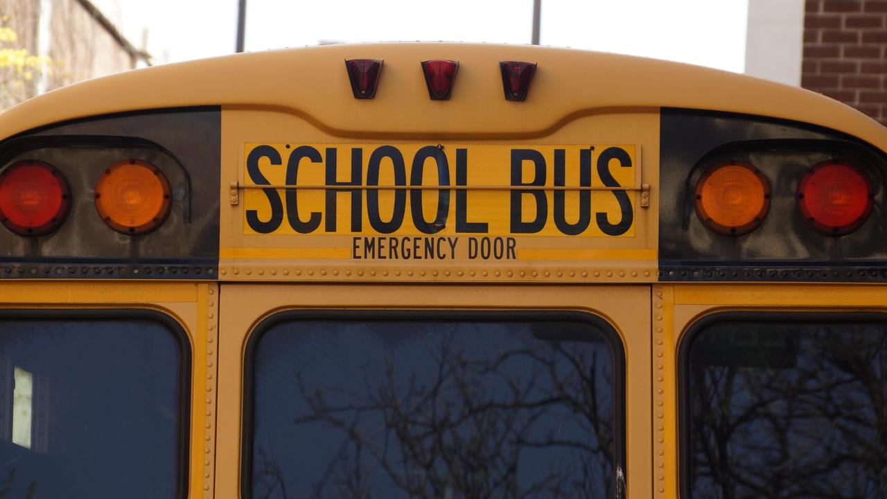 Back view of a yellow school bus displaying the words 'SCHOOL BUS' and emergency door.