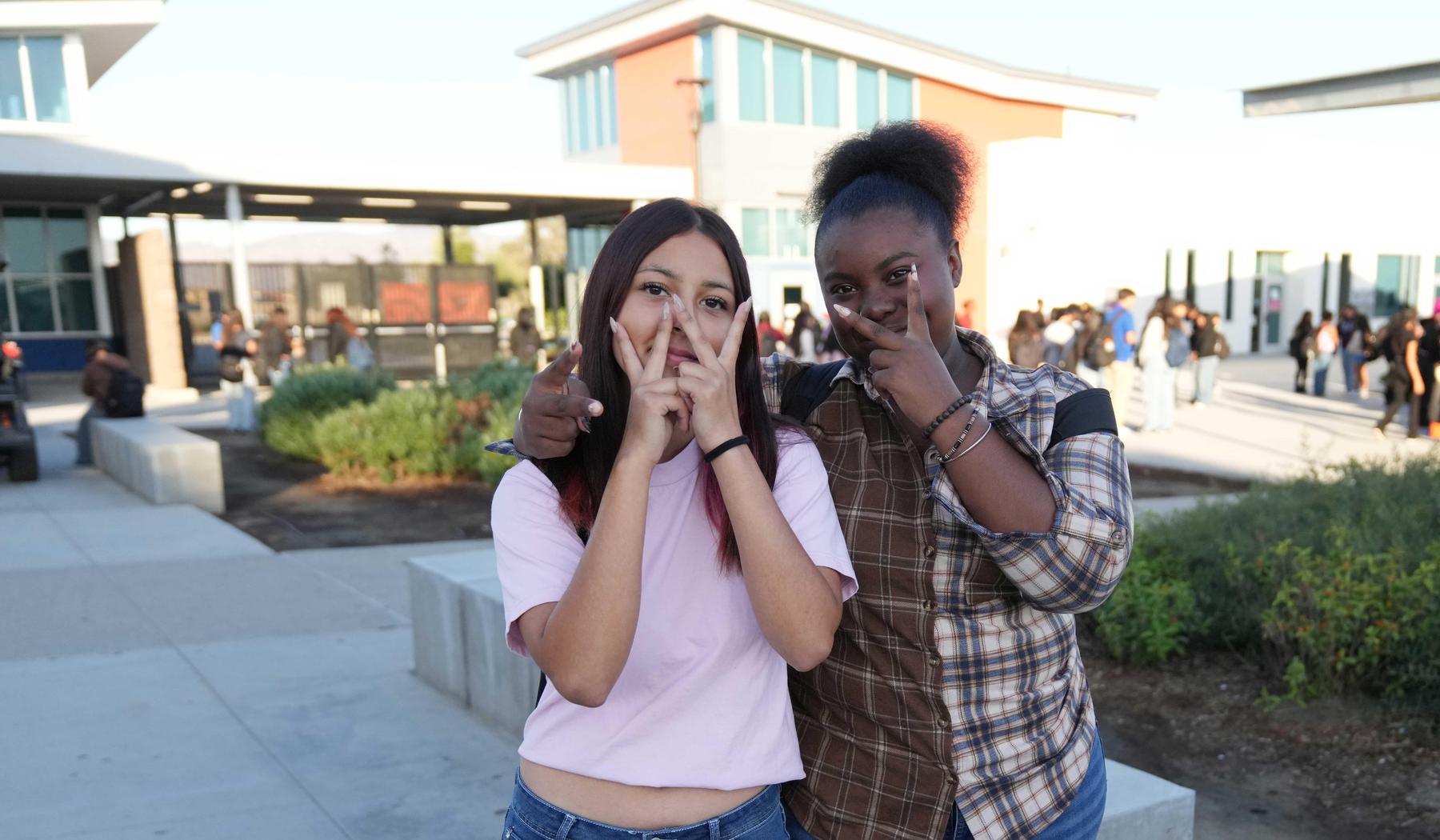 Two friends posing with peace signs outside a school building.