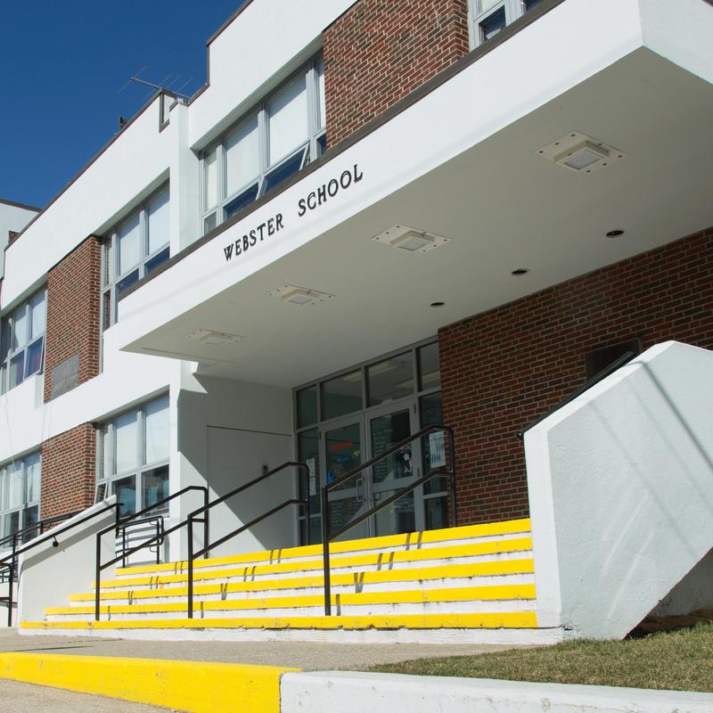 Front view of Webster School showcasing steps and entrance under a clear blue sky.