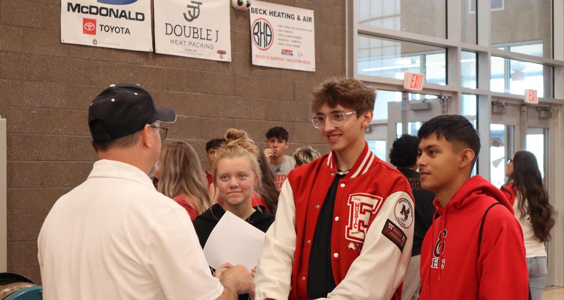 Three students interacting with a man at a school event.