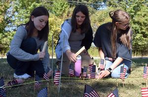Three girls collaboratively organizing tiny flags on a lawn for a remembrance event.