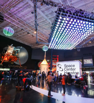 Dark lobby with bright space lights and families standing under a Mars Rover replica