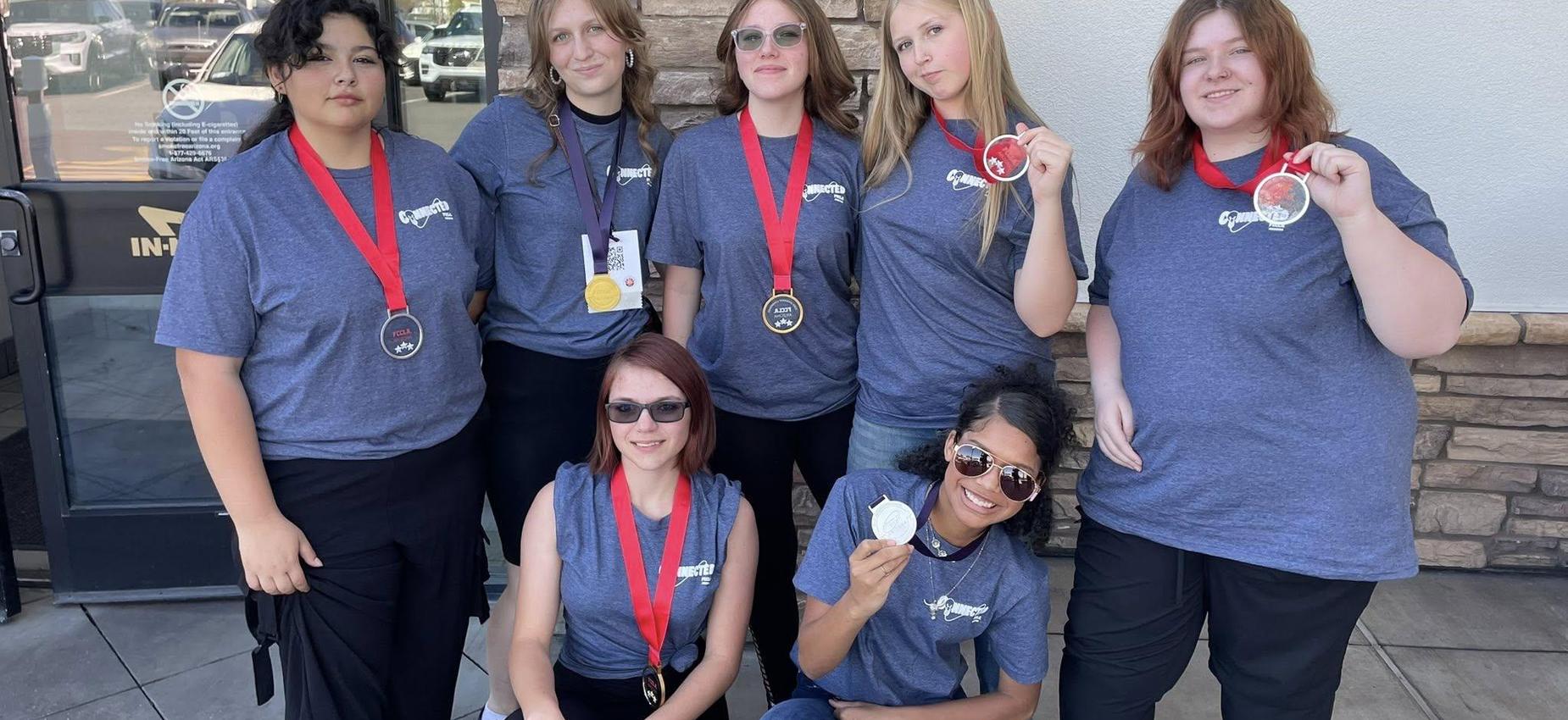 A group of eight individuals wearing matching shirts and medals, posing together outside.