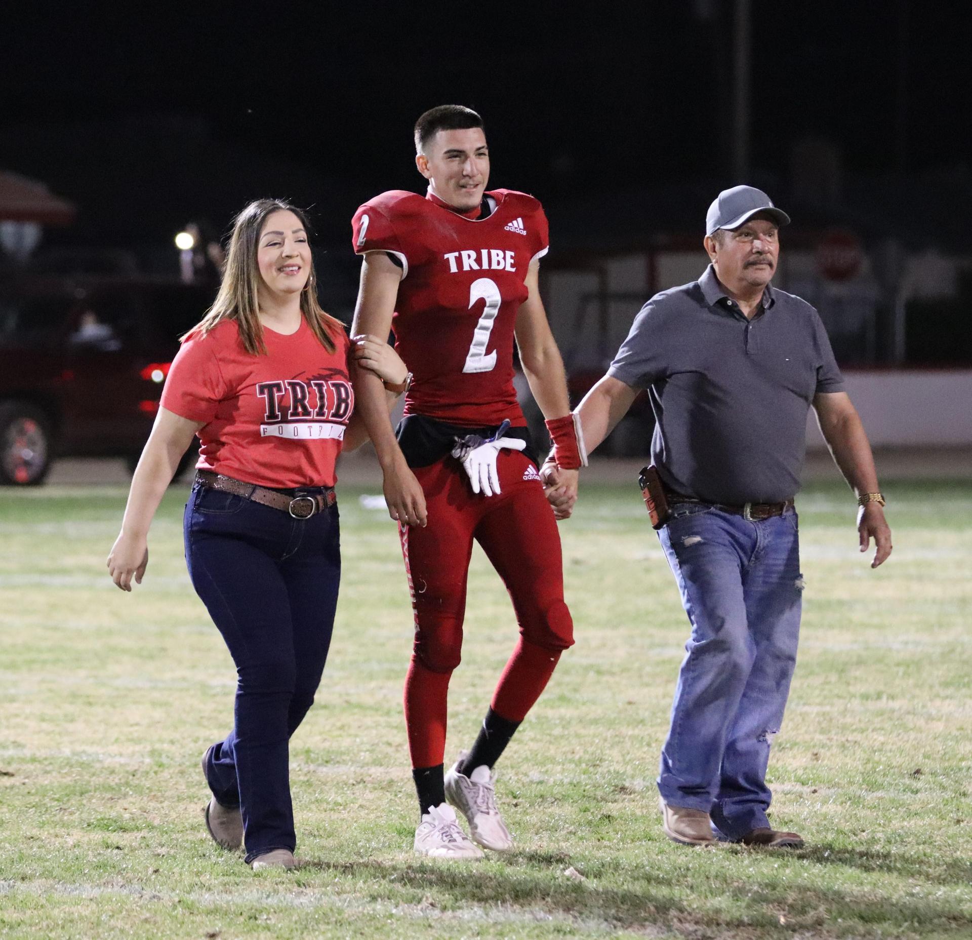 homecoming king and queen candidates walking across the field with their escorts