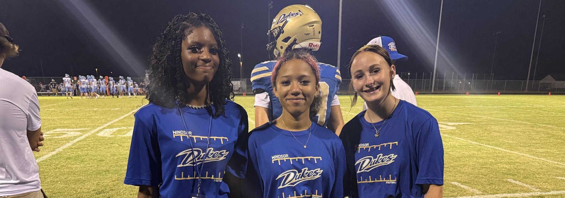 Three individuals in matching blue shirts holding water bottles on a sports field.