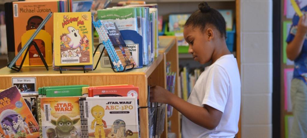 girl looks at books on library shelf