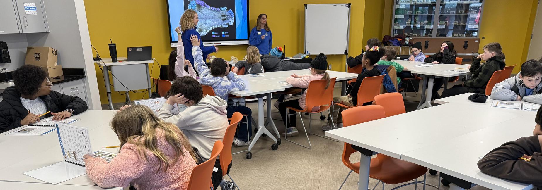Classroom scene with students engaged in activities at individual tables.