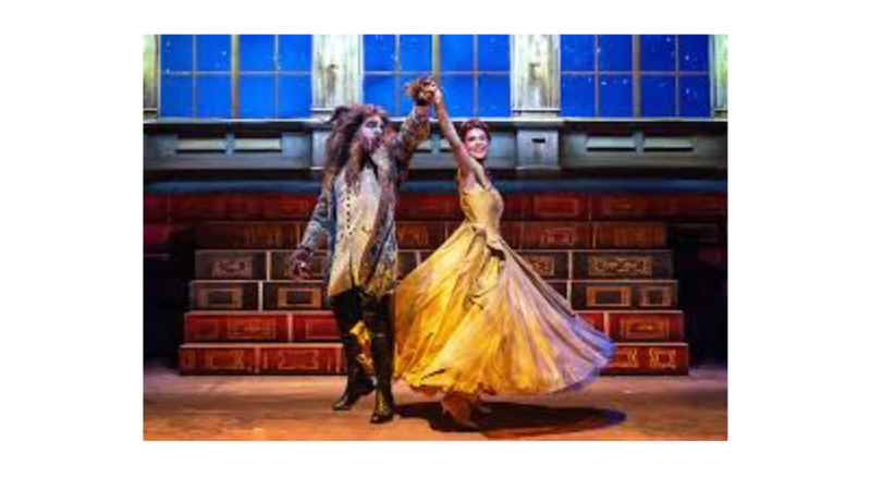 A scene from a musical featuring a lion-like character dancing with a woman in a yellow gown.