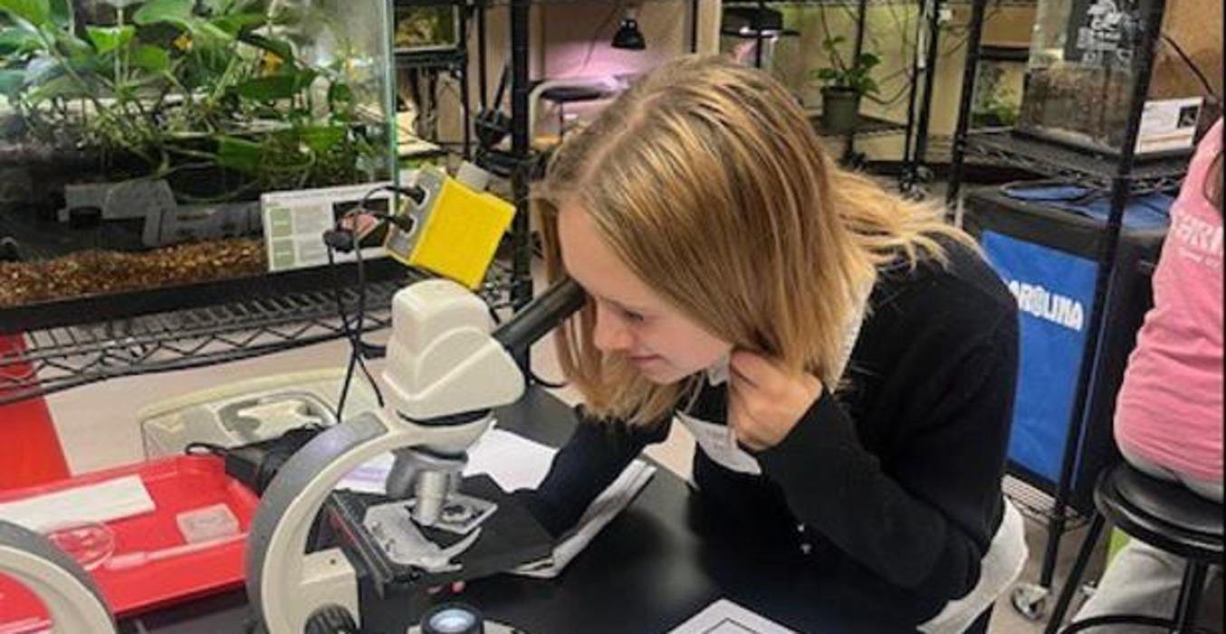 A student studies cells under a microscope.
