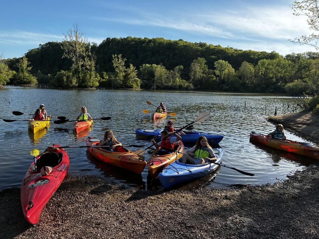 Elementary school students in colorful kayaks on the water.
