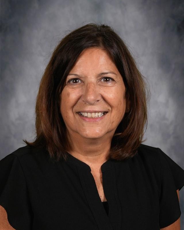 Smiling woman in a black top against a gray backdrop.