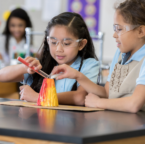 Two girls collaboratively creating a science project with a colorful volcano model.