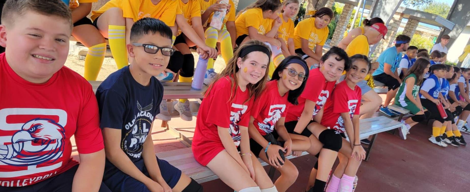 Children in colorful sports jerseys sitting on bleachers, smiling and chatting.